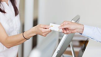 Die Krankenkassen übernehmen alle Schutzimpfungen und manche Krankenkassen auch noch weitere Ein Mann gibt einer Rezeptionistin seine Krankenkassenkarte